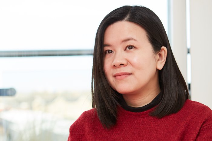 Jacqueline, diagnosed with diffuse large b-cell lymphoma, looks beyond camera in a red jumper.