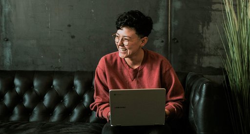 A woman sitting on a chesterfield sofa types on a laptop.