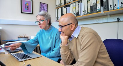 Two people sitting at a desk discussing research findings on a laptop screen.