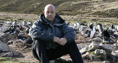 Edward, a retired soldier who was diagnosed with myeloma, sitting on a rock on a hiking trail looking straight faced at the camera.
