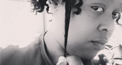Black and white photograph of Simone, with medium length curly hair, looking serious and pulling at one curl.