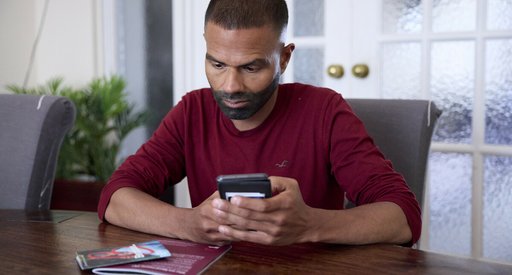 A man sitting at a table, with Blood Cancer UK booklets in front of him. He's holding his phone, as if about to search for something or dial a number.